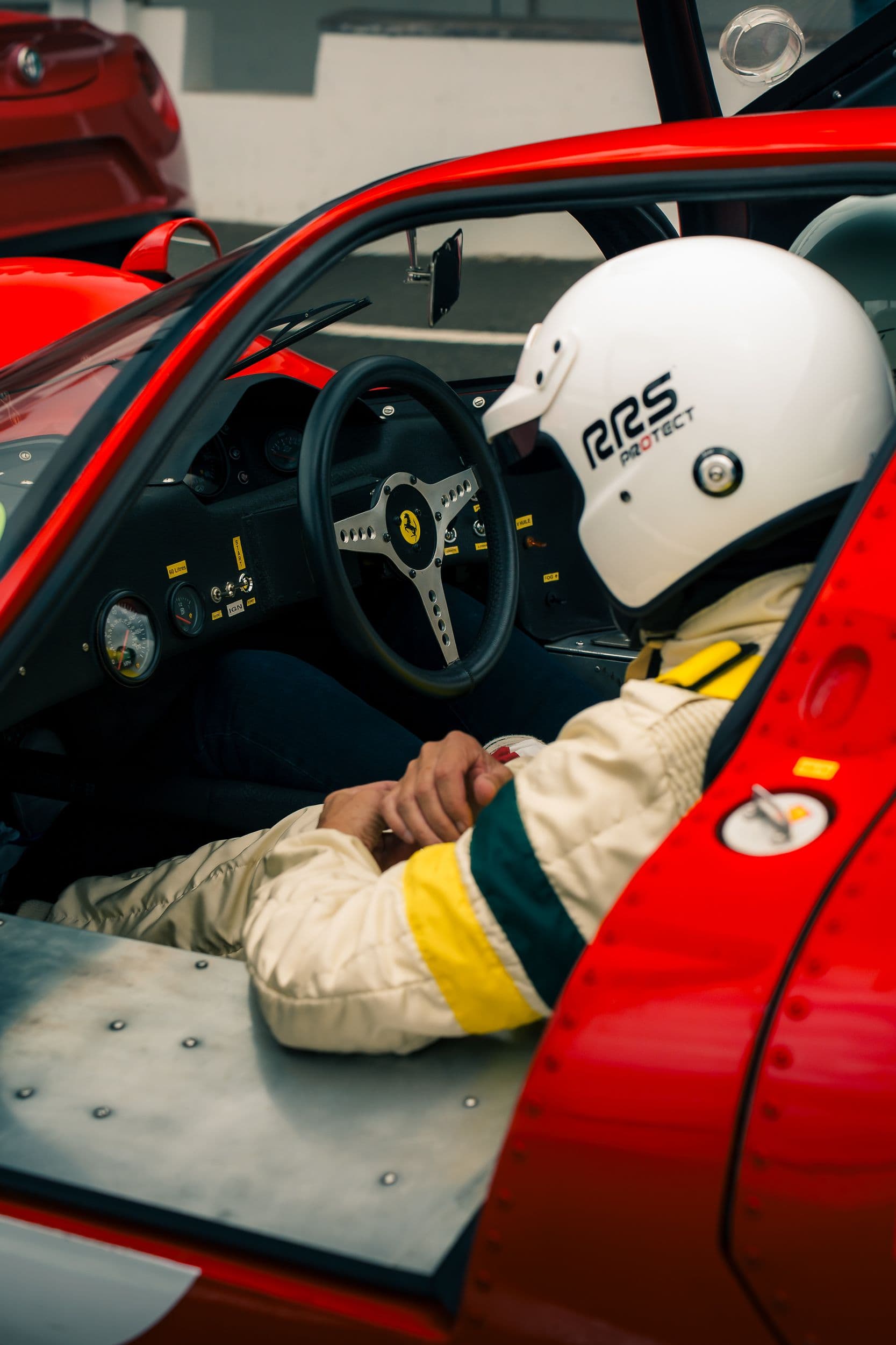 Occupant au casque blanc dans l’habitacle d’une Ferrari 330 P4 Replica, près du volant et des compteurs.