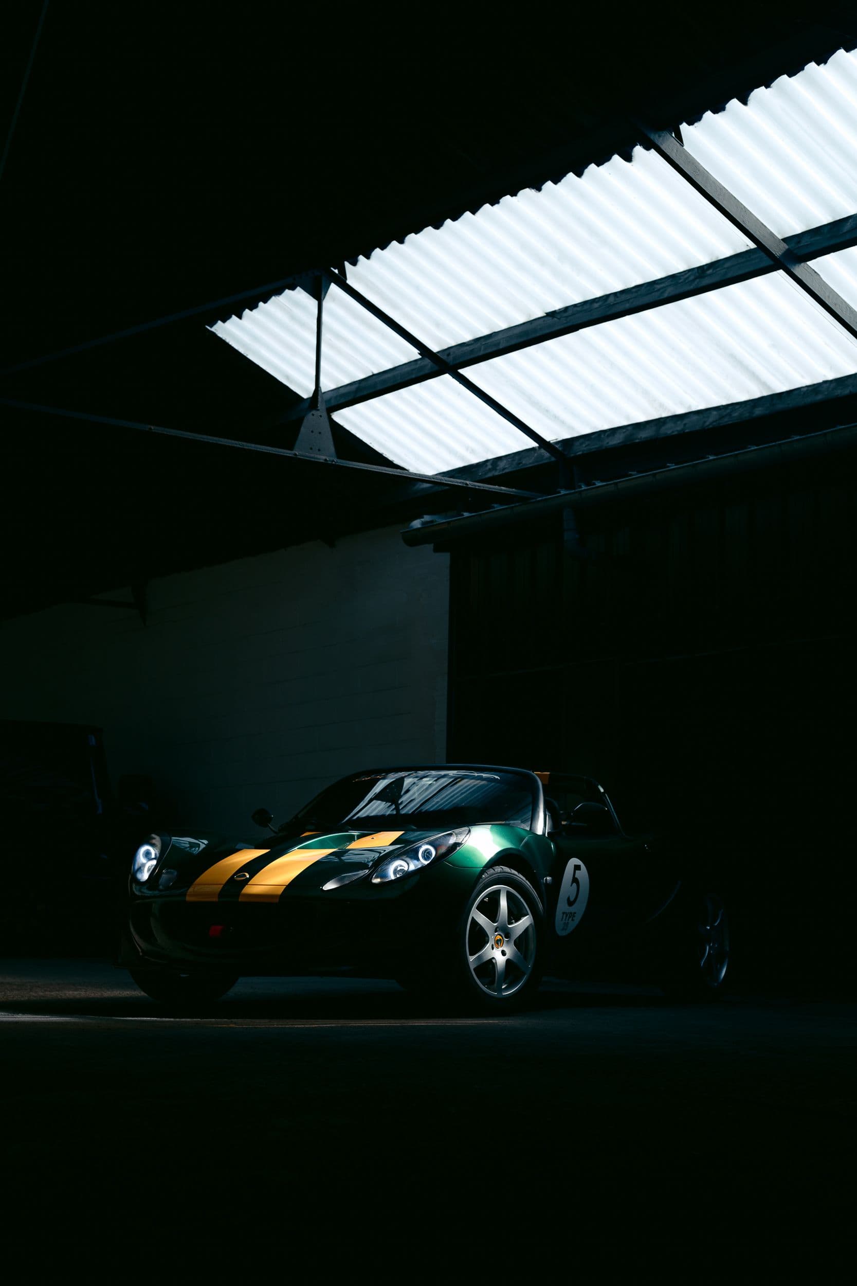 Lotus Elise S2 verte à bandes jaunes, vue trois-quarts avant sous verrière d’atelier