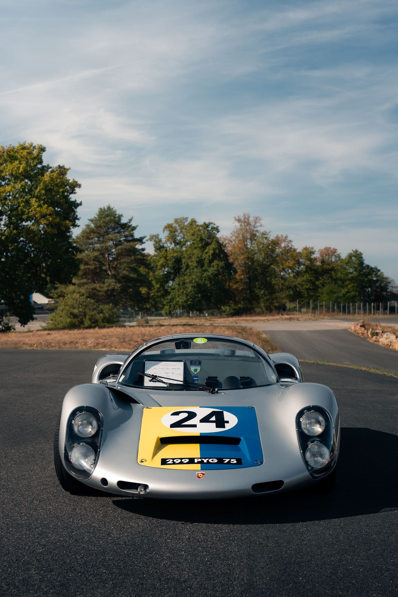 Porsche 910 argentée vue de face, avec numéro 24 sur un capot jaune et bleu.
