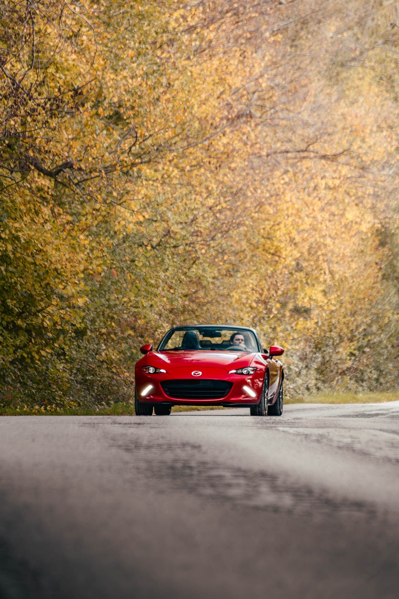 Mazda MX-5 roadster rouge sur route forestière d'automne avec conducteur au volant, photographie cinématographique