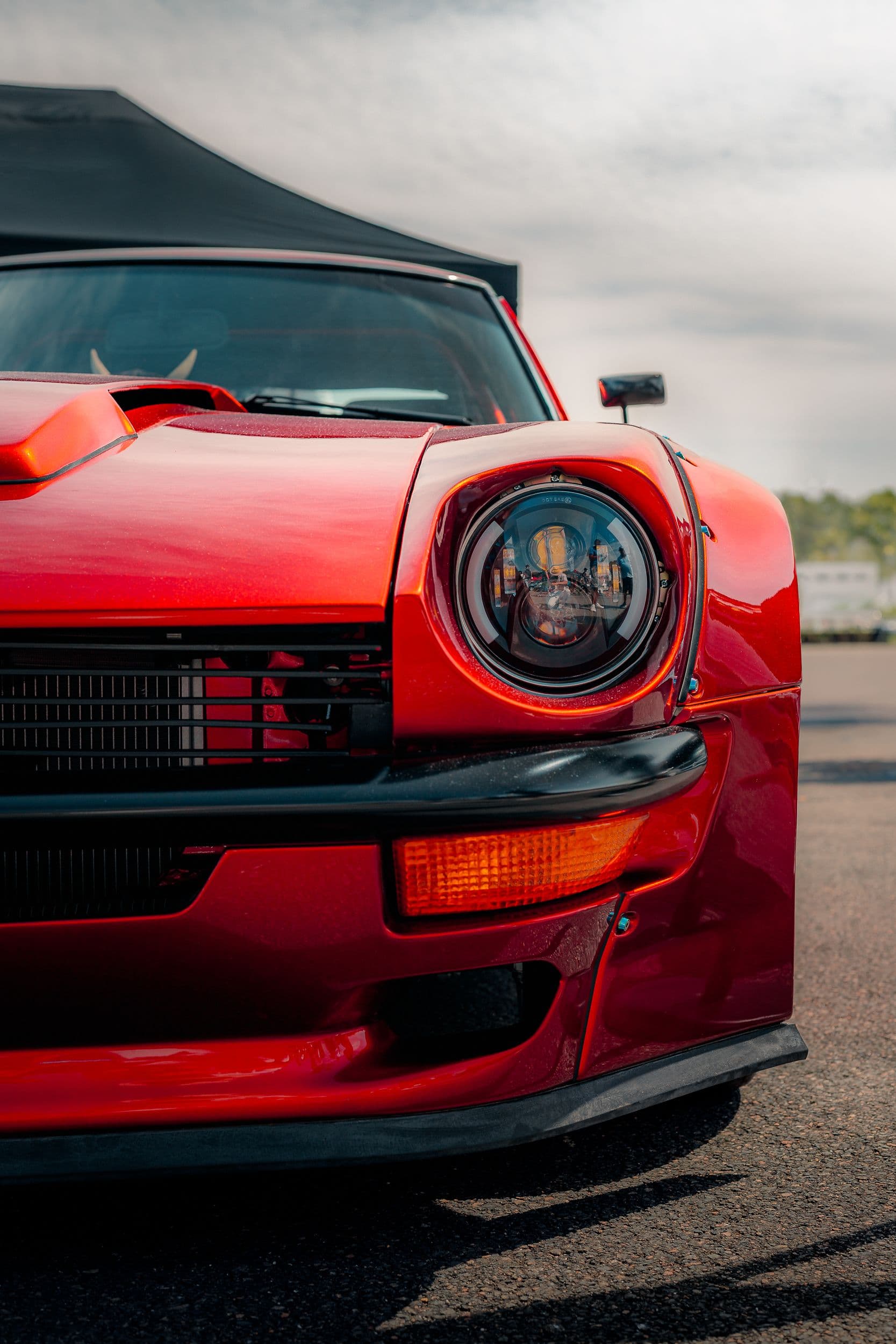 Gros plan du phare avant d’une Datsun 260Z rouge, reflets et calandre en arrière plan.