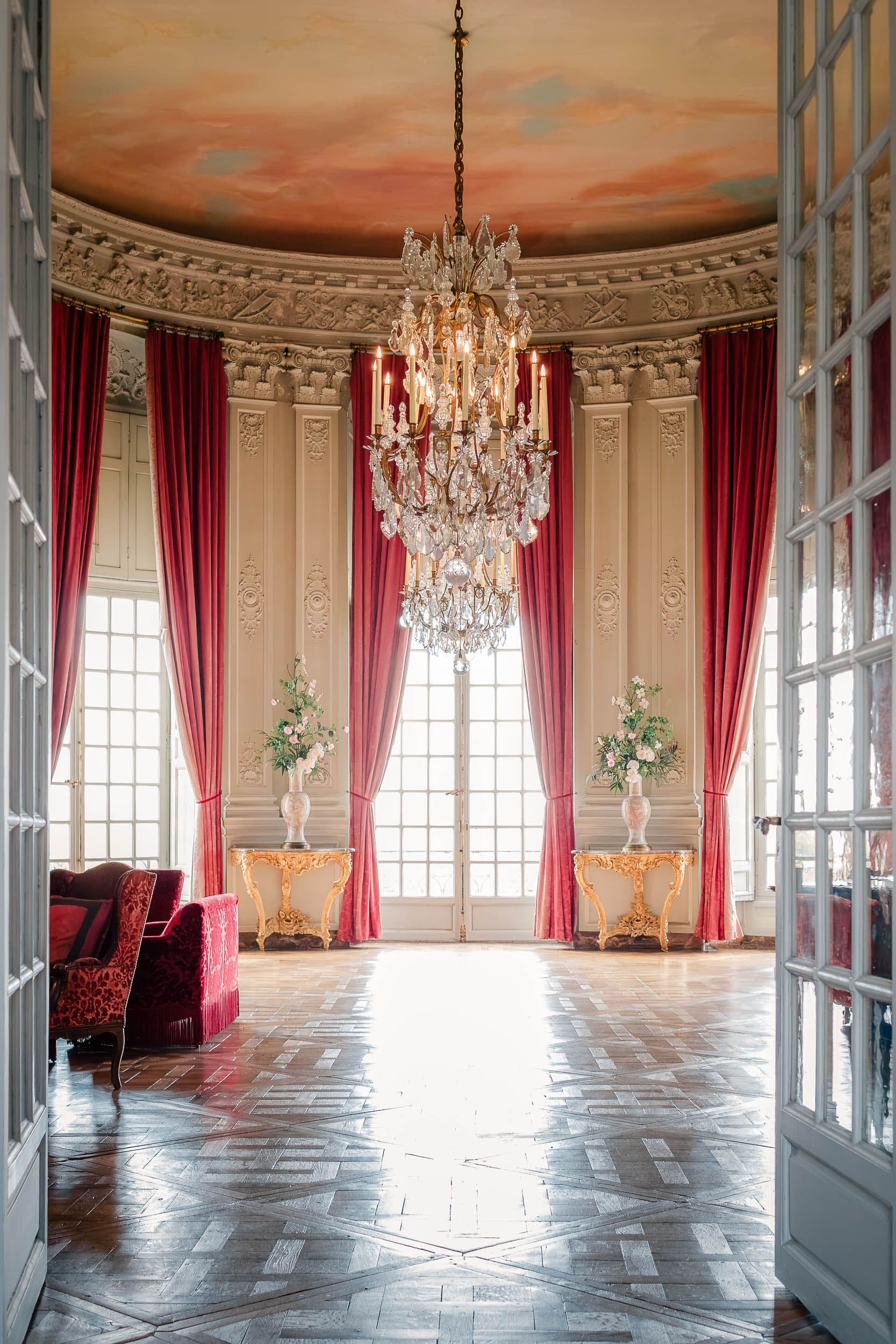 Salon ovale avec plafond peint, lustre en cristal monumental et rideaux roses, architecture XVIIIe siècle