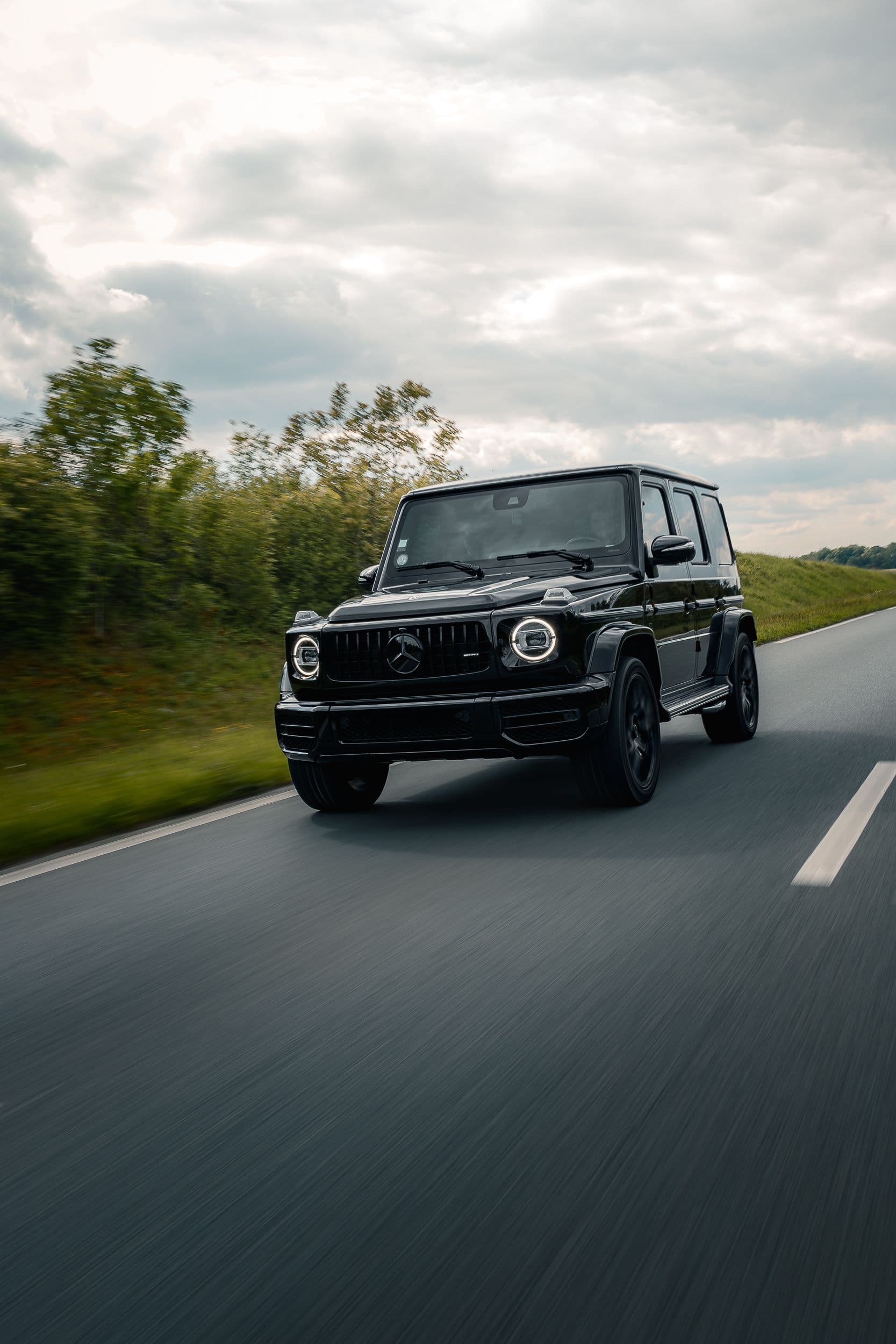 Mercedes G63 AMG noir en roulage de face, sur route dégagée en pleine campagne.