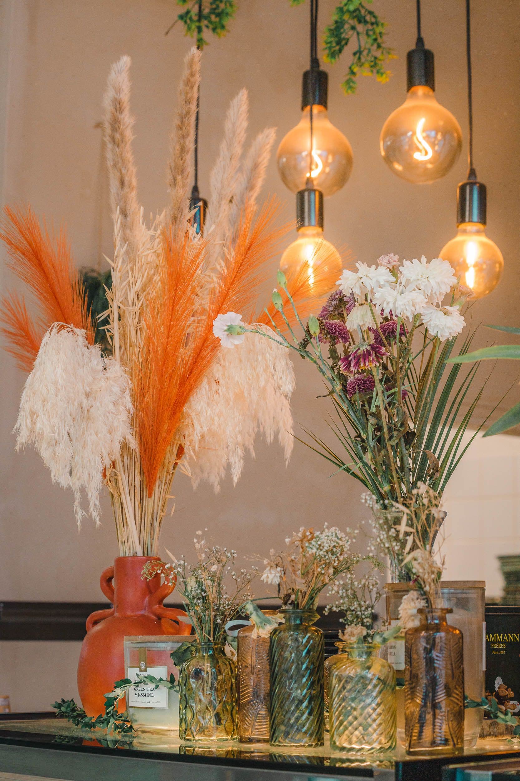 Composition décorative avec fleurs séchées orangées, bougies et suspensions pour identité visuelle de coffee shop