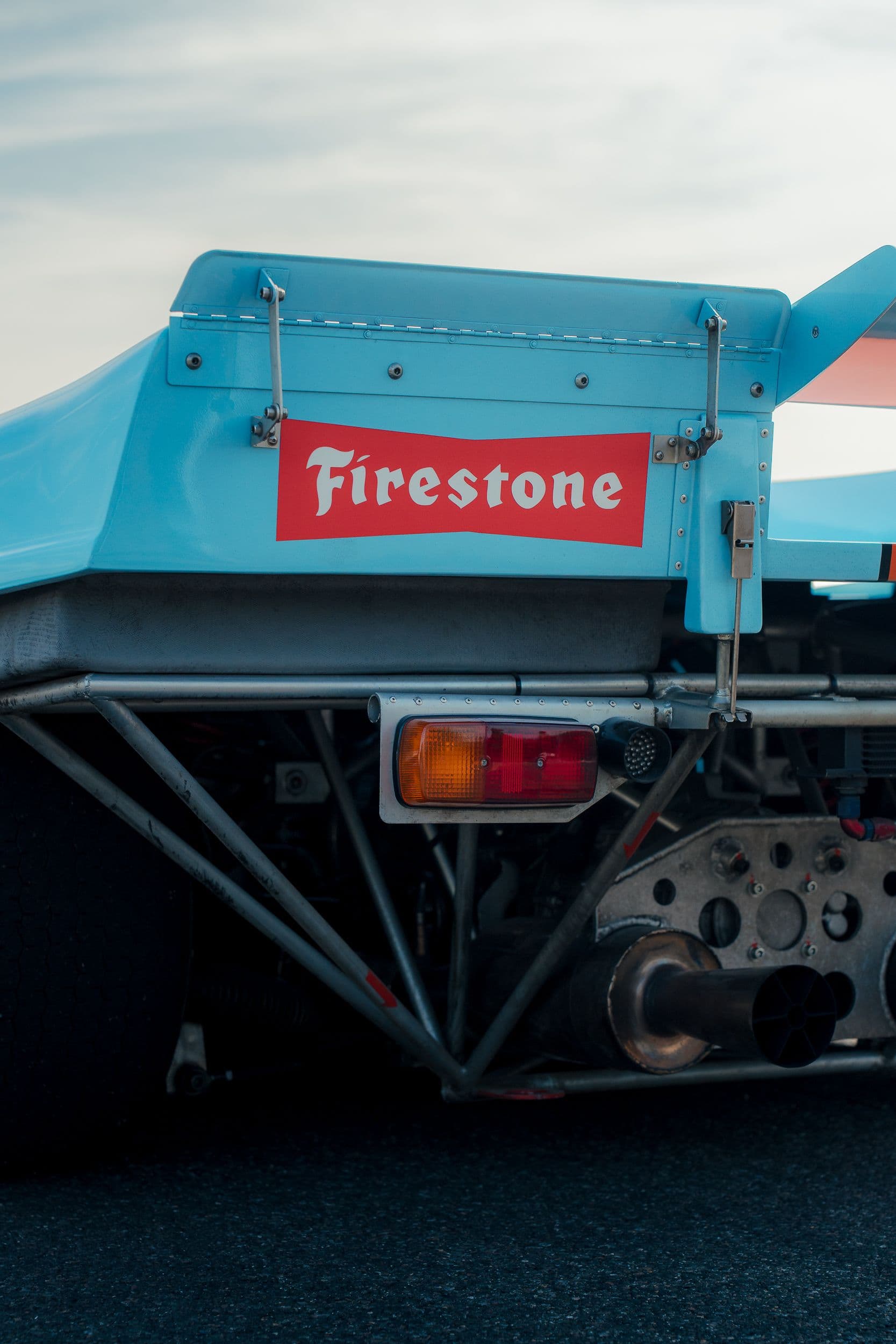 Arrière d’une Porsche 917 Replica, avec logo Firestone, feu rectangulaire, structure tubulaire et échappement visibles.