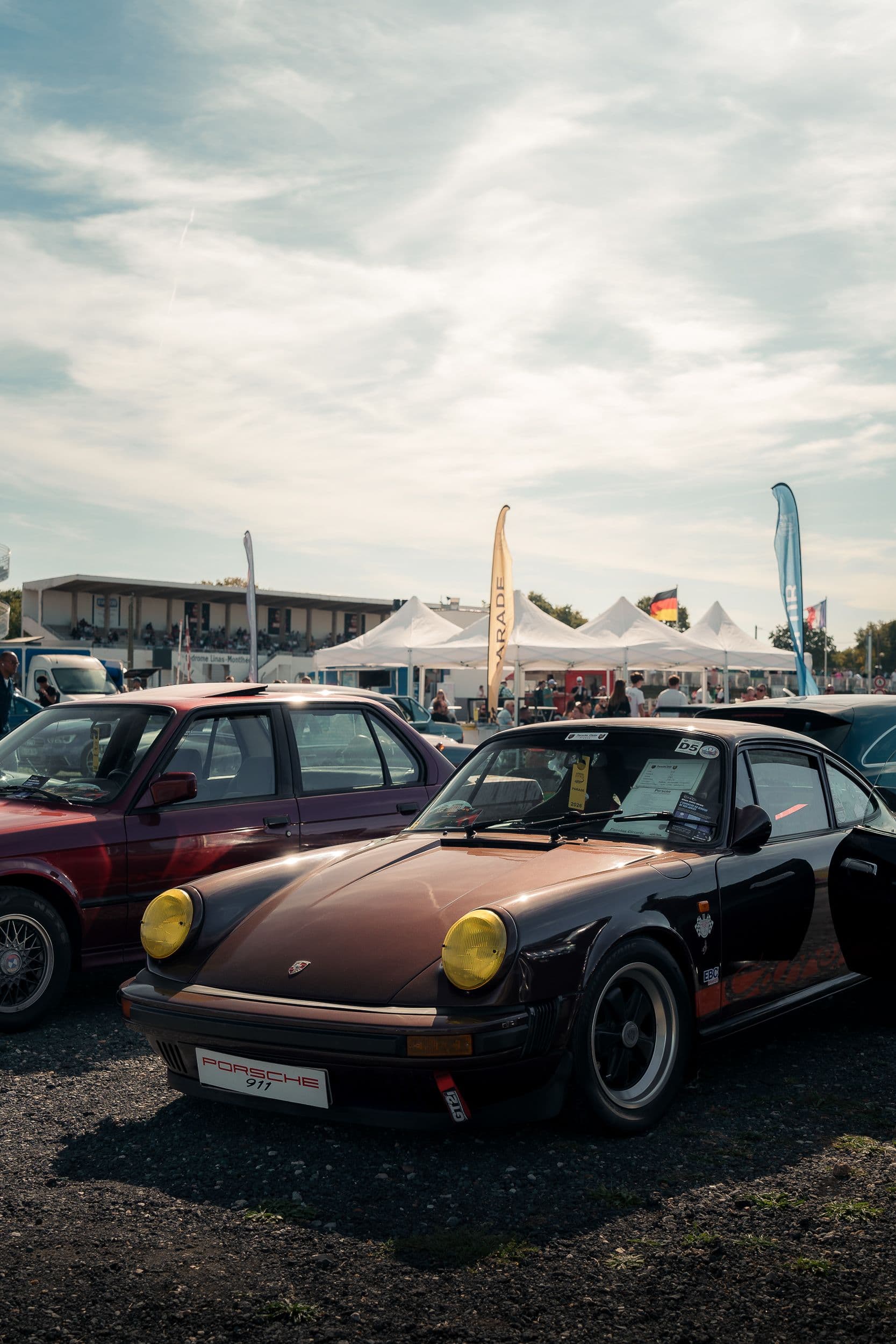 Porsche 911 classique marron exposée parmi les voitures du rassemblement.