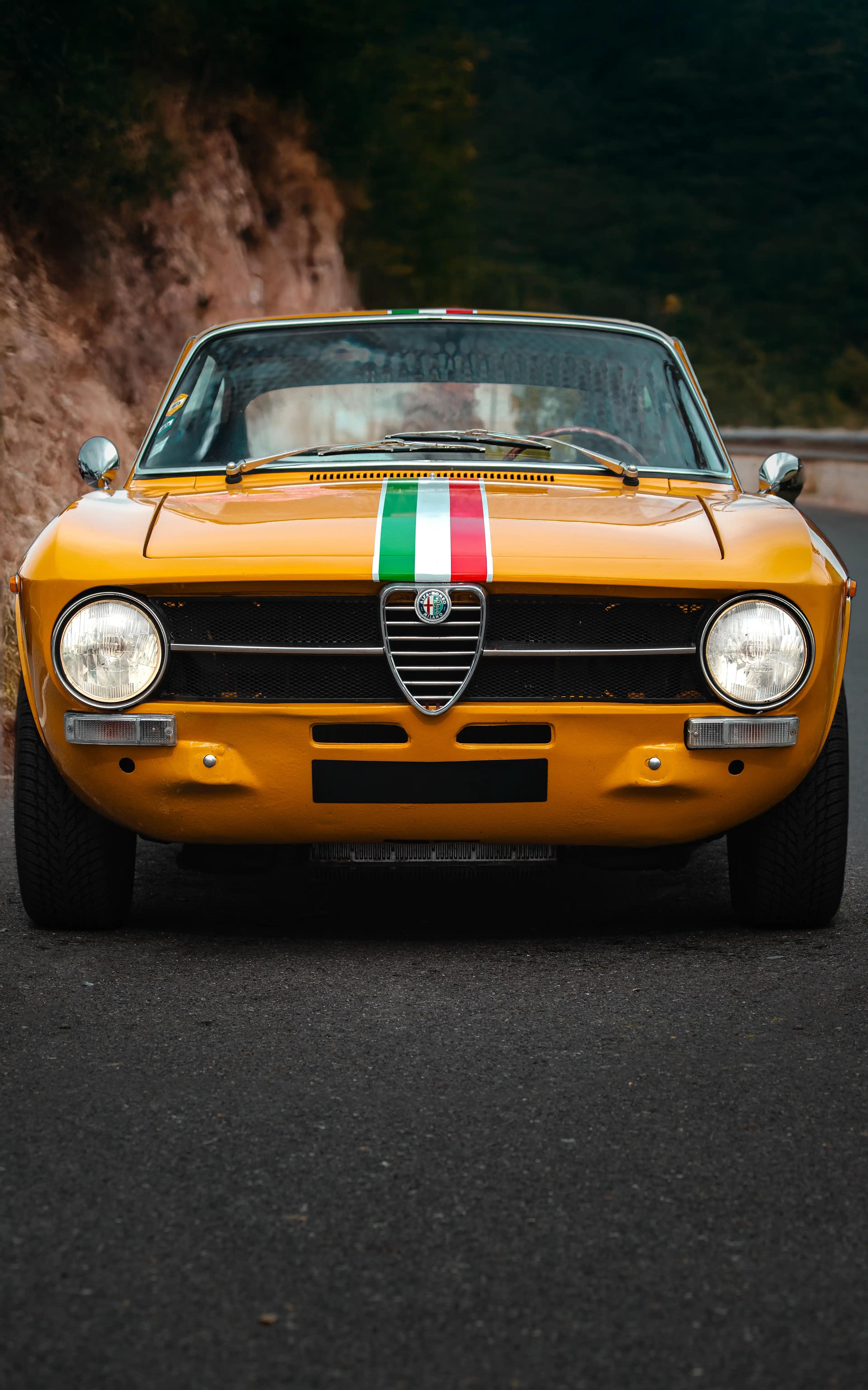 Vue avant de l'Alfa Romeo GT1300 Junior jaune sur route, photographie automobile classique.