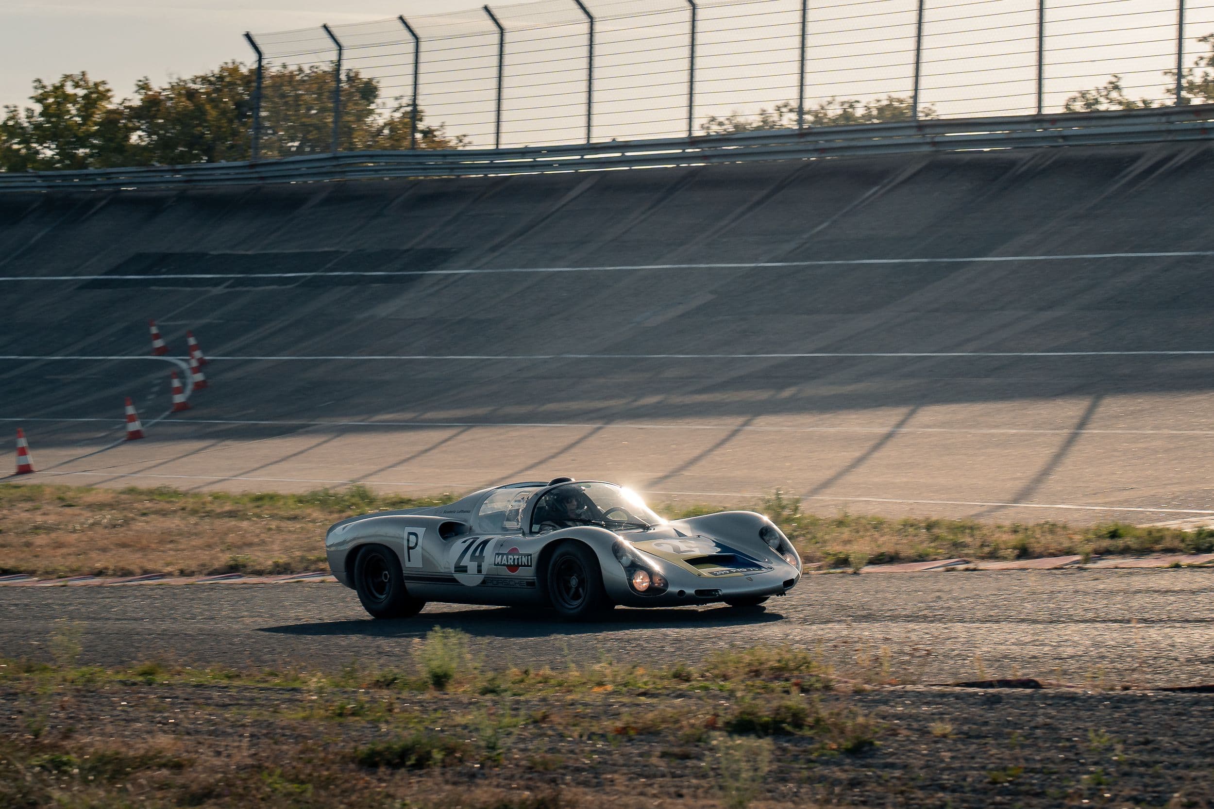 Porsche 910 argentée roulant en contre-jour au pied du virage relevé de Montlhéry.