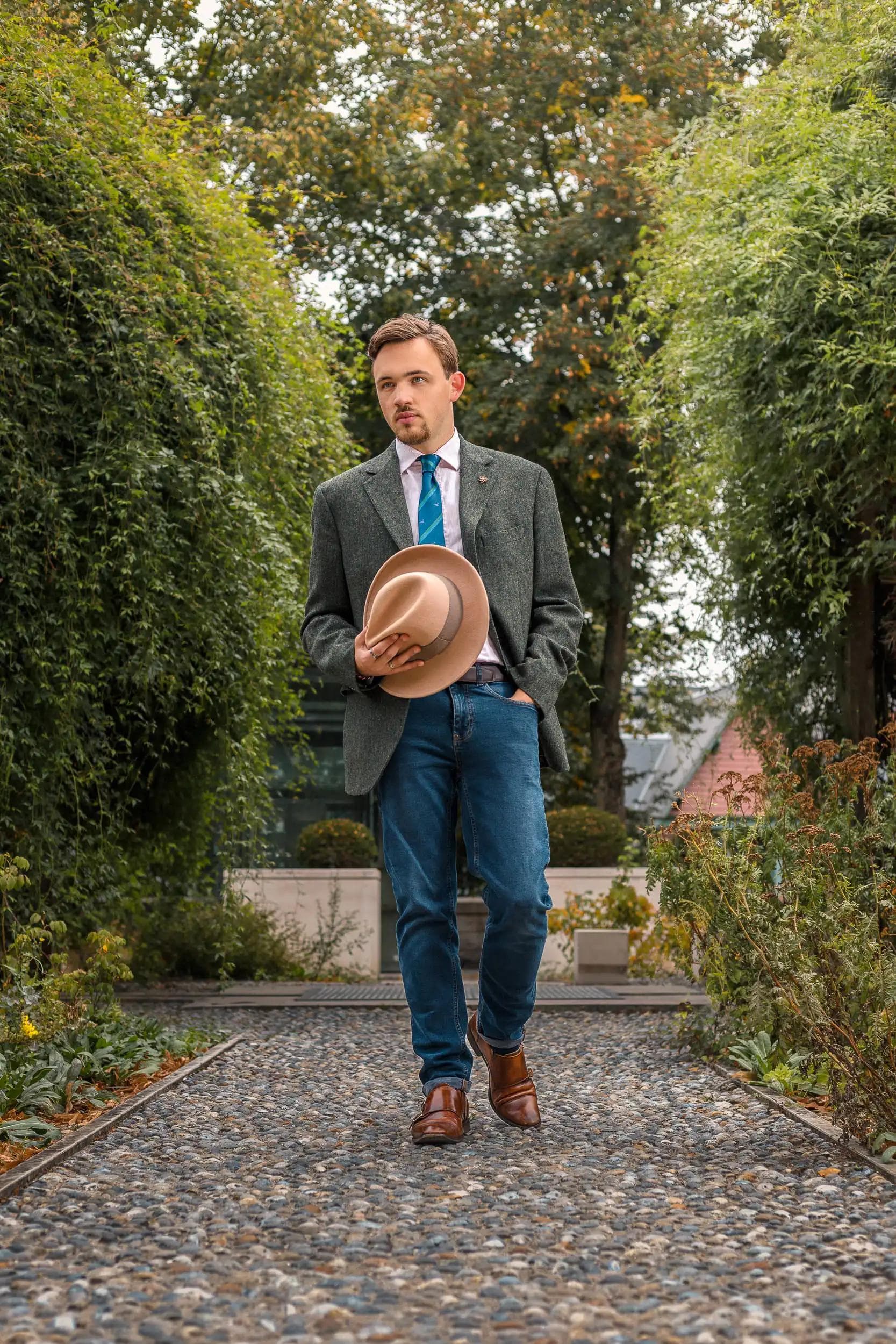 Portrait mode d’un homme tenant son chapeau en marchant dans un jardin à Amiens, réalisé par le photographe Arthur Monteil dans un style éditorial naturel.