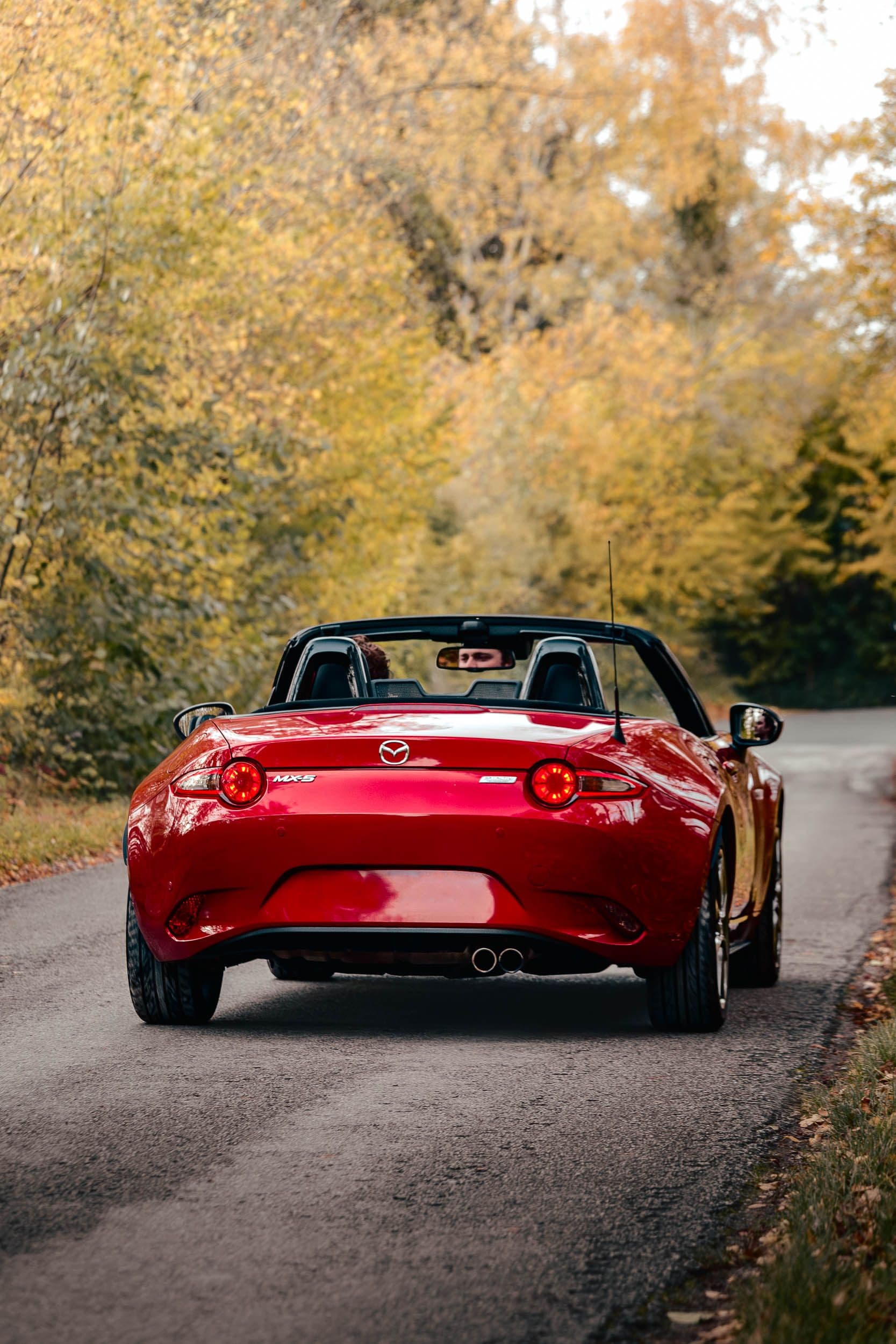Vue arrière de la Mazda MX-5 roadster rouge avec feux allumés sur route d'automne, photographie narrative Arthur Monteil