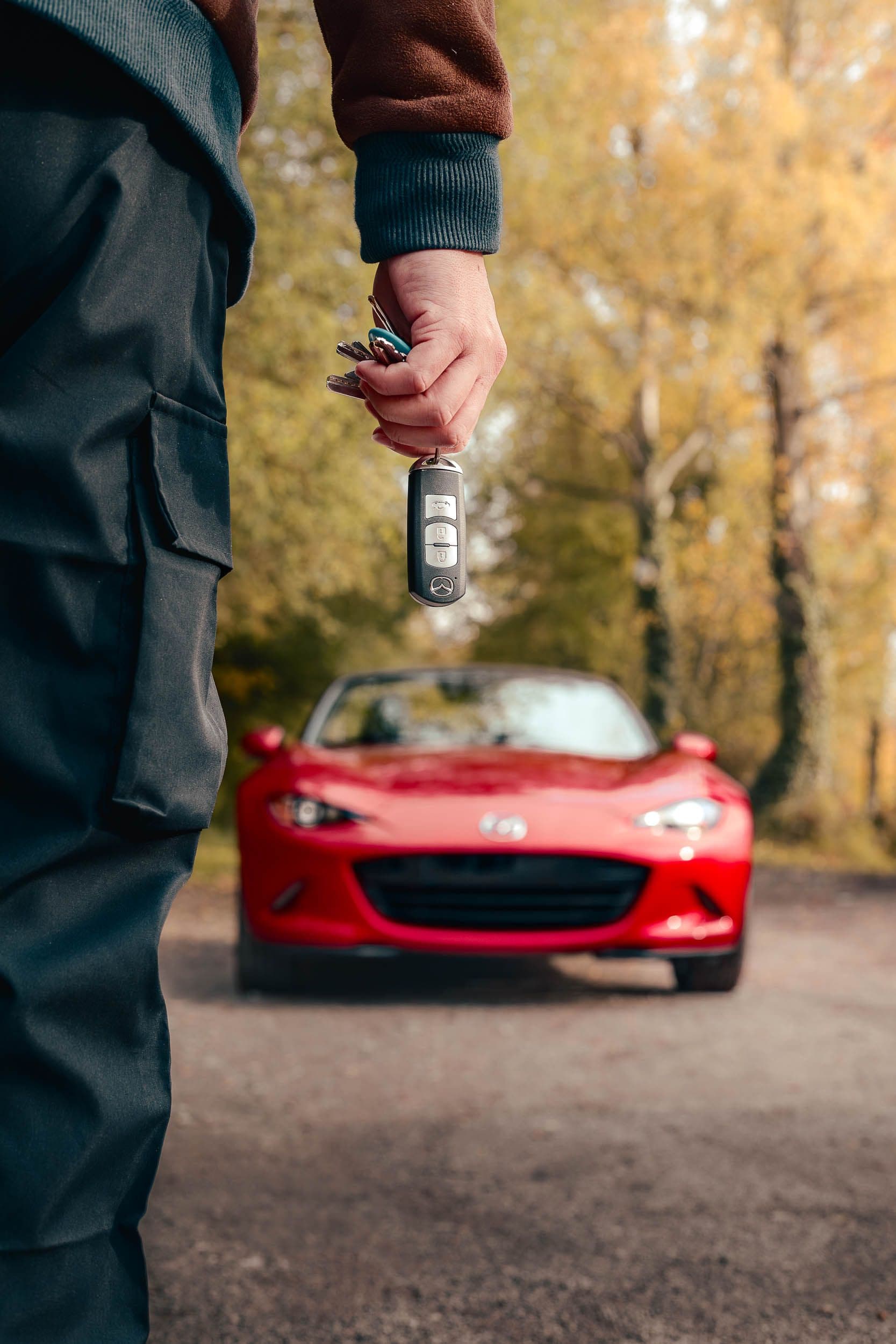 Main tenant les clés de la Mazda MX-5 rouge floue en arrière-plan, symbolisant la philosophie Jinba ittai de connexion