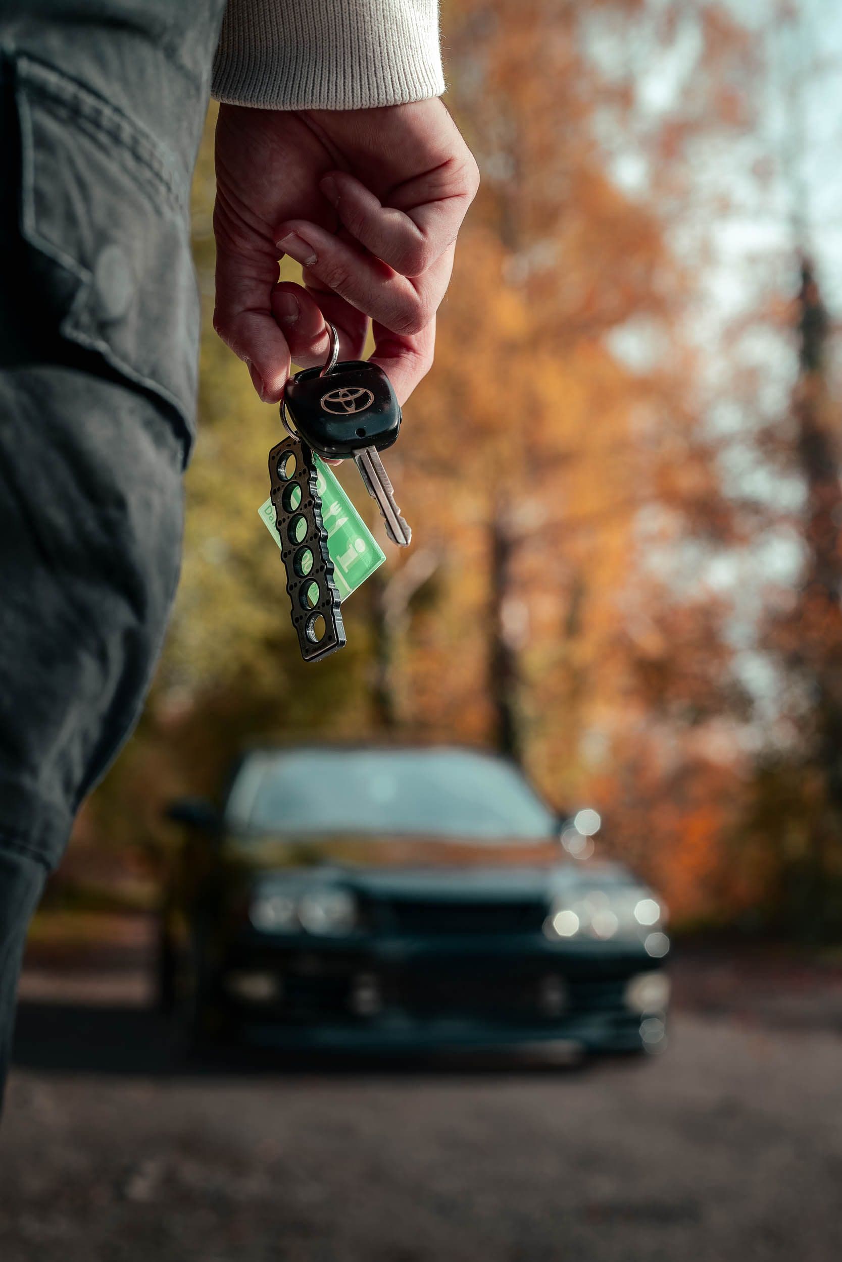 Main tenant clés Toyota avec Chaser JZX100 en arrière-plan flou, photographie lifestyle automobile automne, berline JDM
