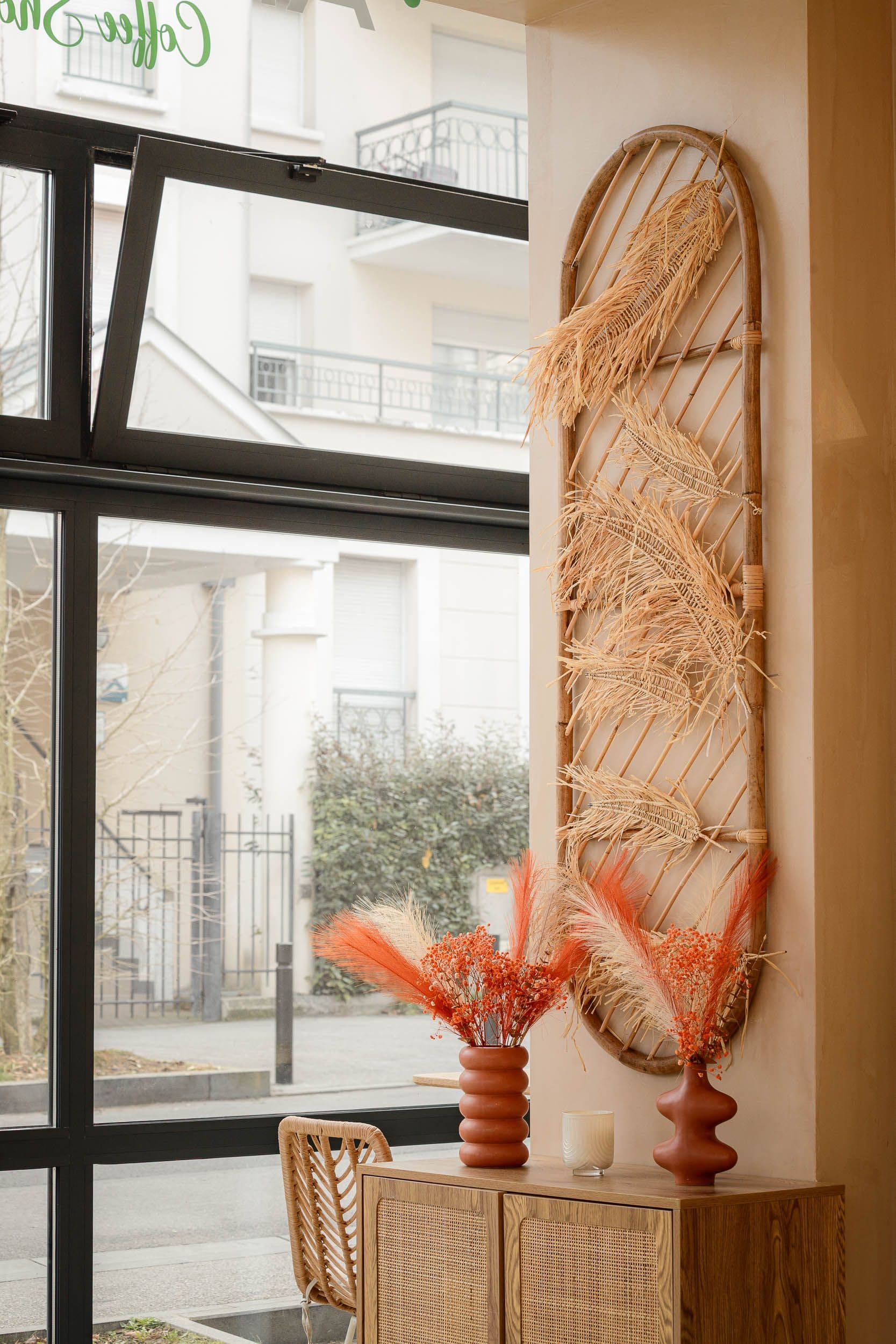 Décoration murale en rotin avec fleurs séchées orangées et mobilier bois dans un coffee shop, photographie d'architecture d'intérieur
