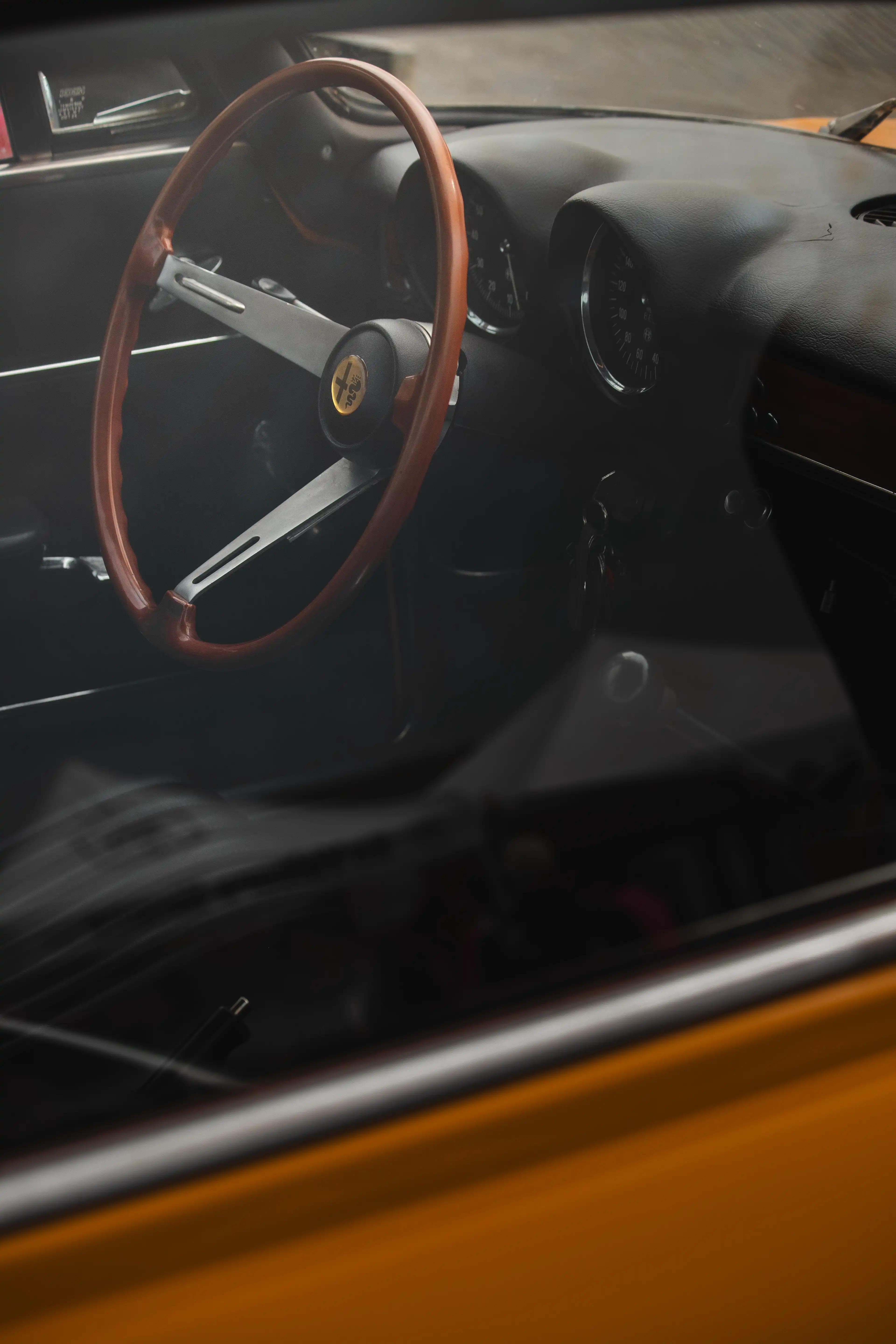 Vue intérieure de l'Alfa Romeo GT1300 Junior à travers la vitre, volant bois et compteur vintage.