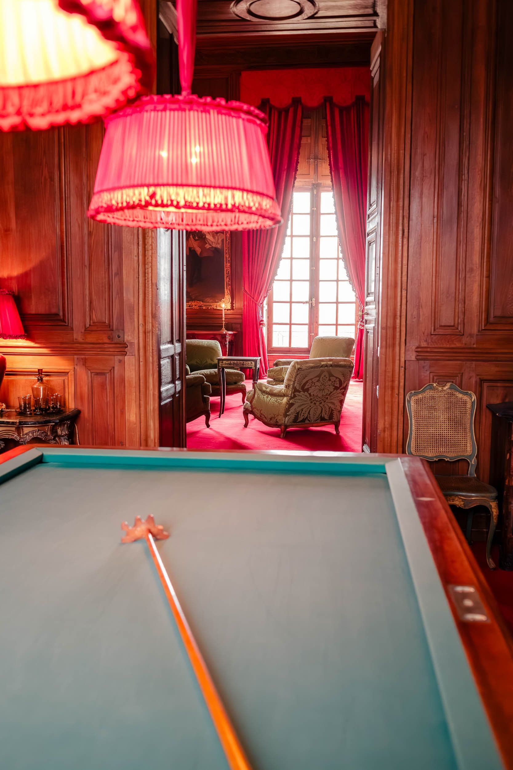 Salle de billard avec boiseries en acajou, fauteuils verts et lampes roses, atmosphère cosy château français