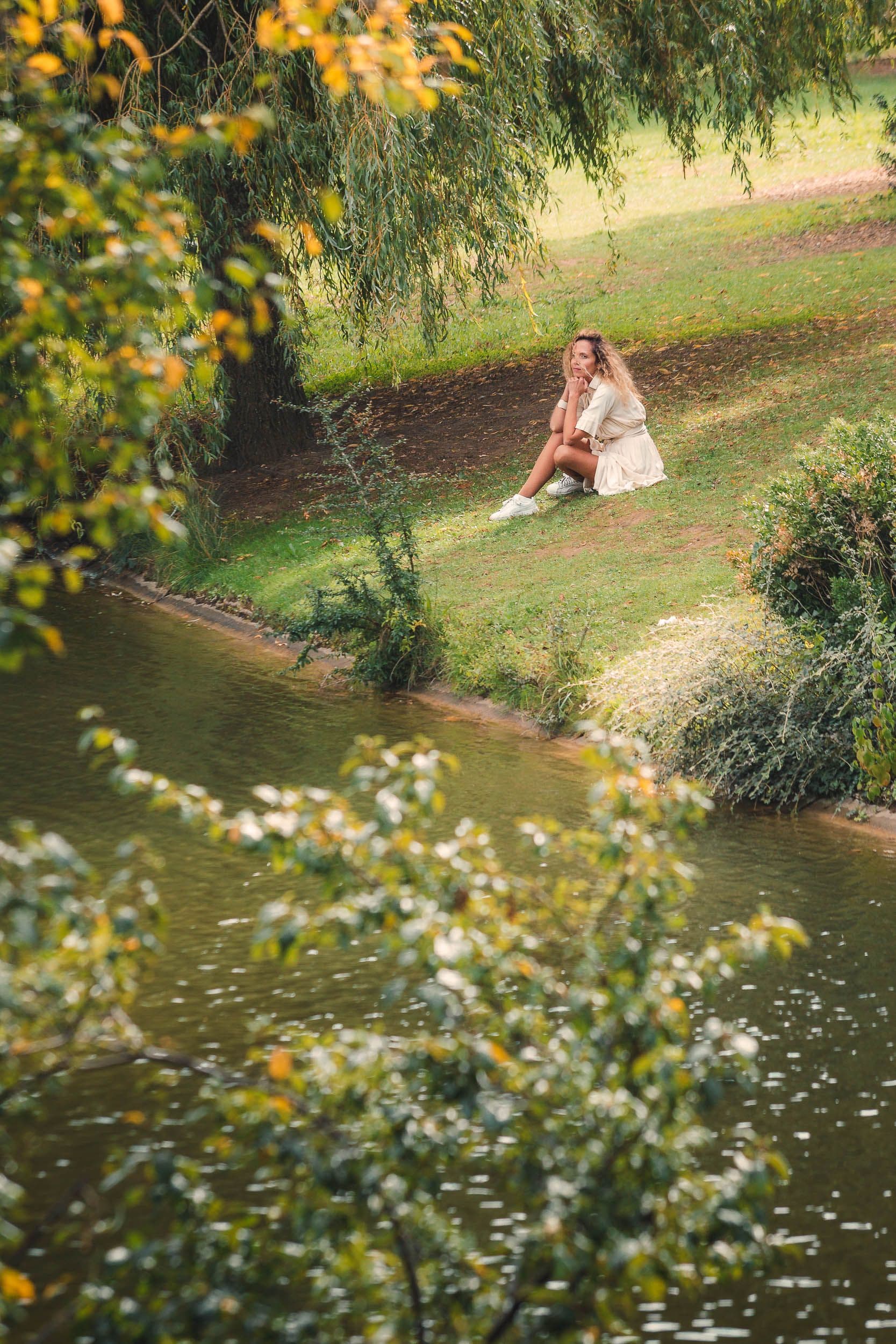 Silhouette assise au bord d’un étang, captée au milieu de la végétation.