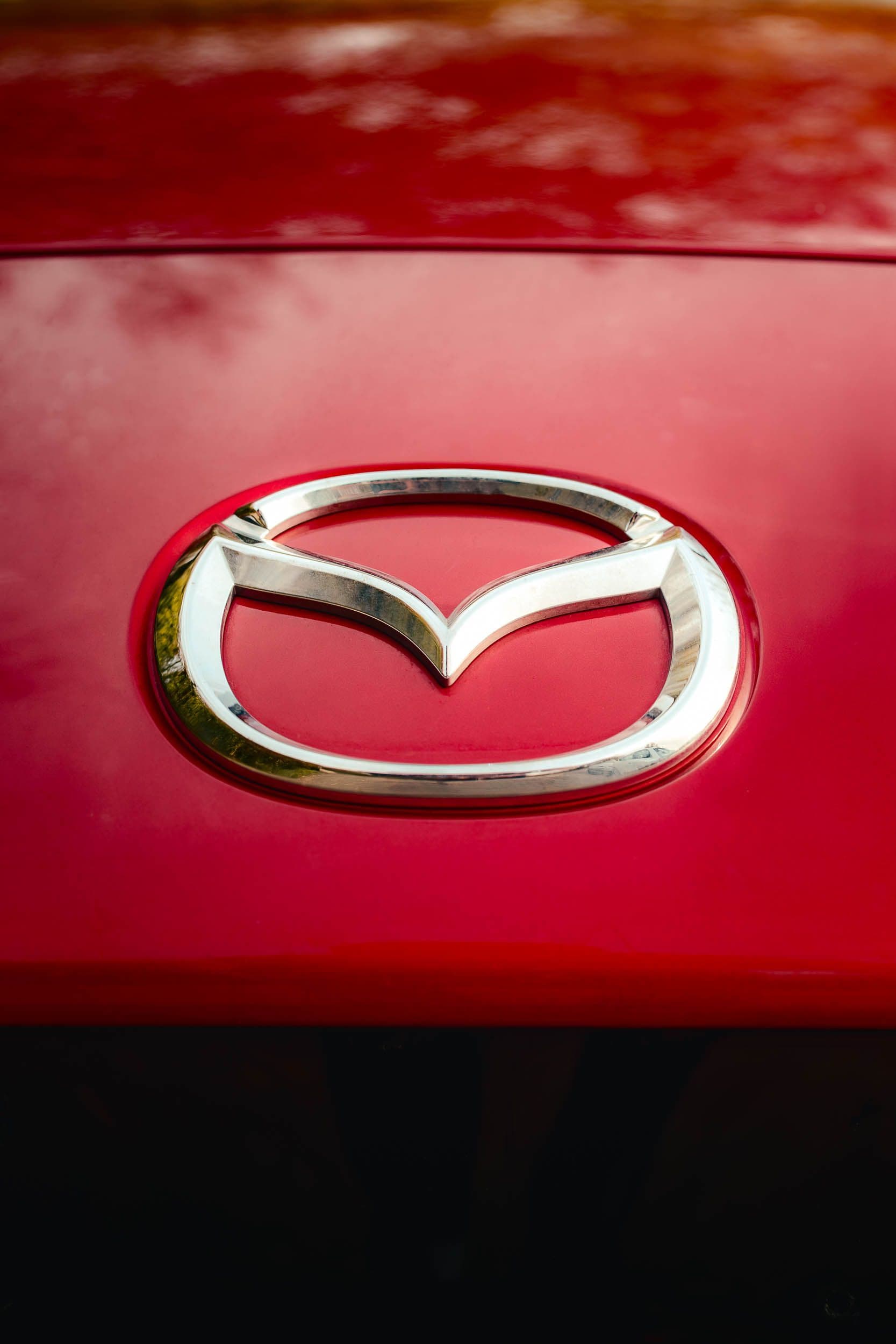 Gros plan du logo Mazda chromé sur carrosserie rouge, photographie de détail automobile premium