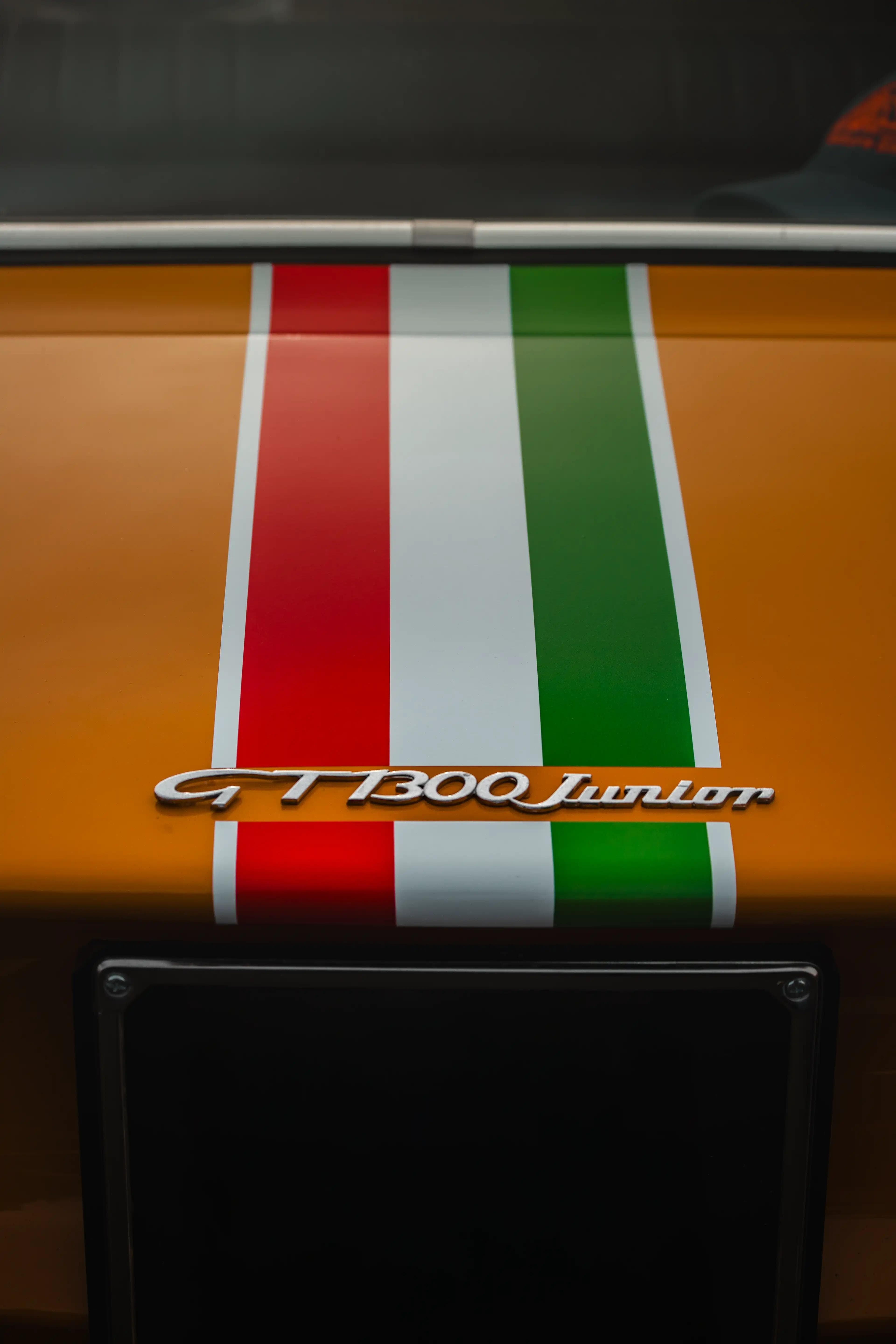 Détail du badge GT1300 Junior avec bandes italiennes sur capot, photographie automobile classique.