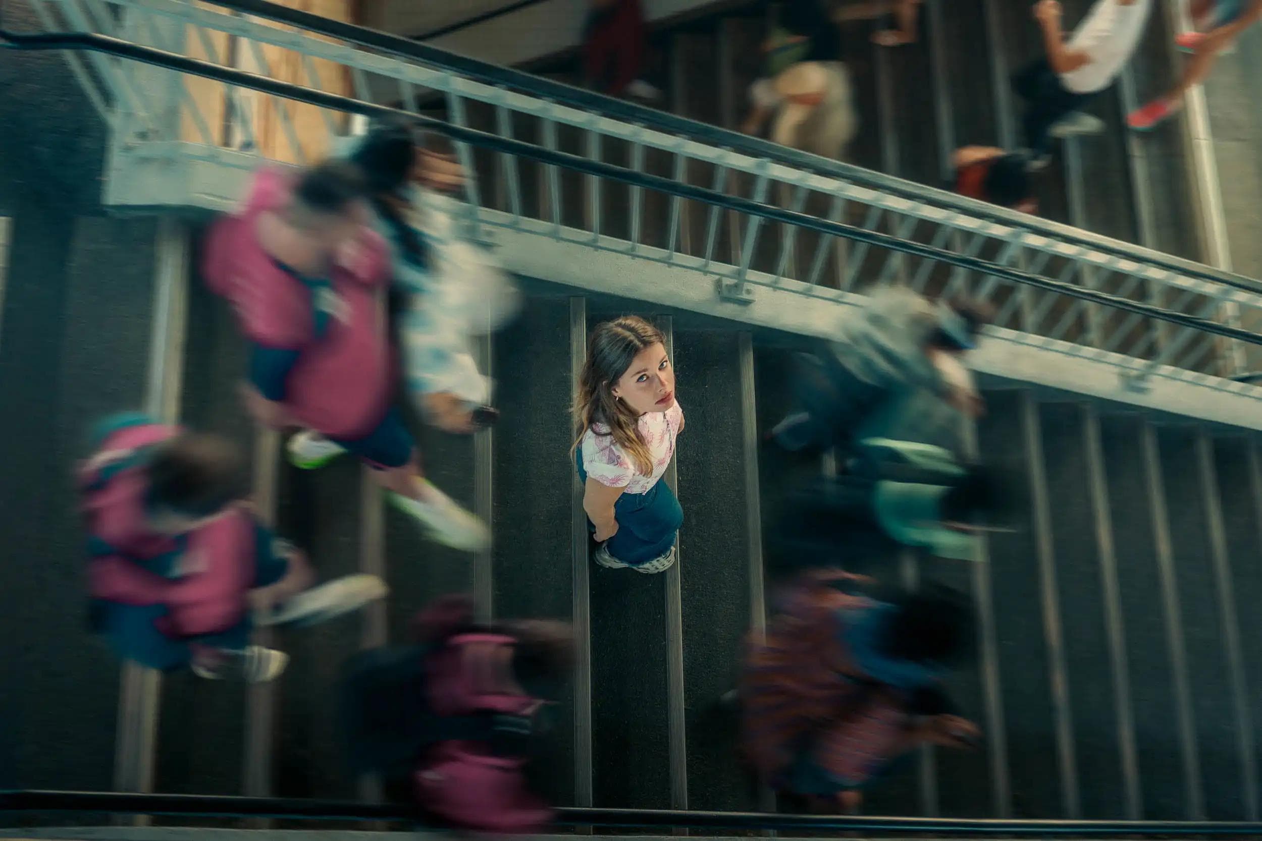 Vue en plongée d’une femme immobile au centre d’un escalier entourée d’une foule en mouvement, scène cinématographique réalisée à Paris par Arthur Monteil pour illustrer l’introspection façon Inception.
