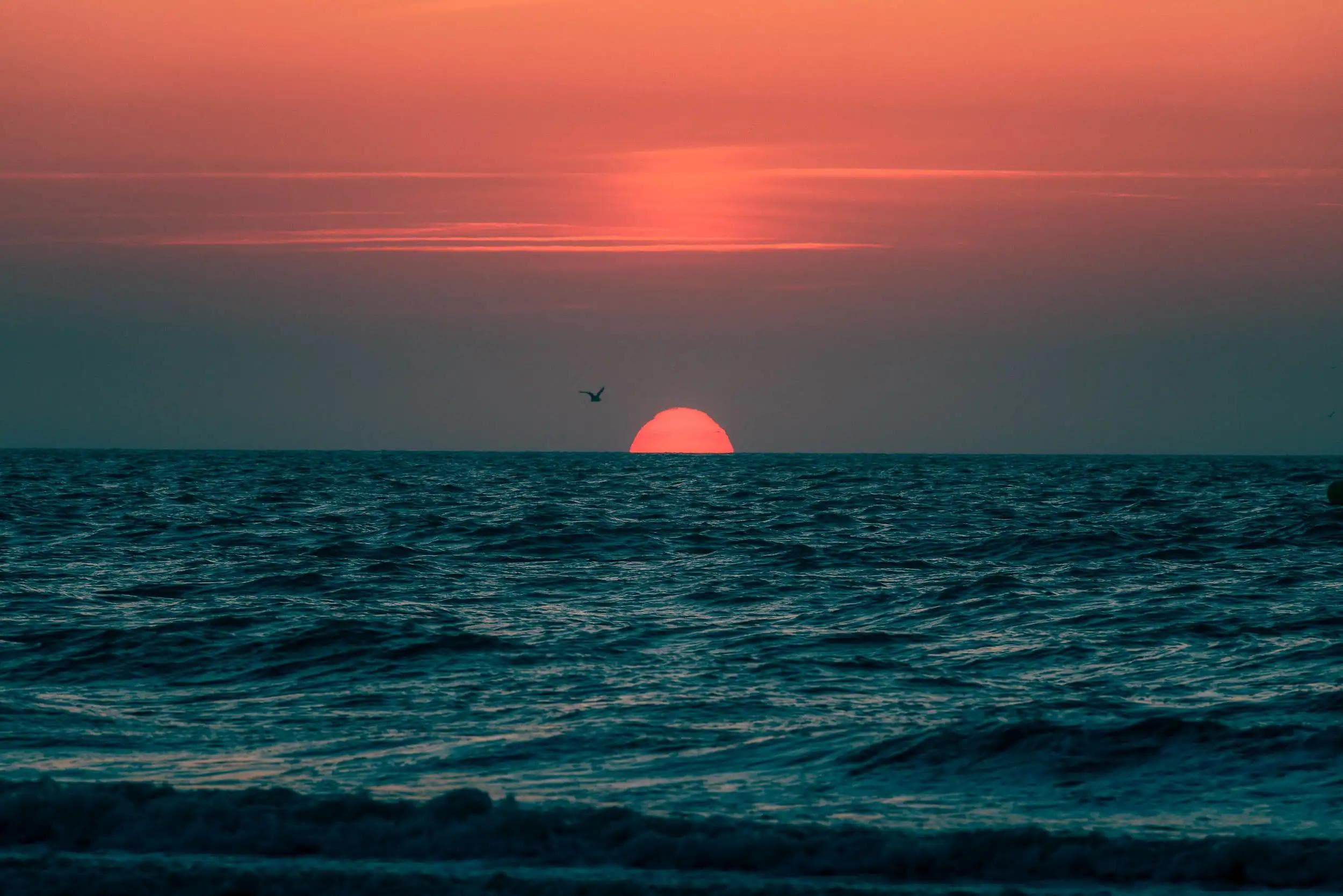 Le soleil à moitié immergé sous l’horizon au-dessus de la mer à Deauville, dans une atmosphère rouge et bleu profond, photographie par Arthur Monteil.