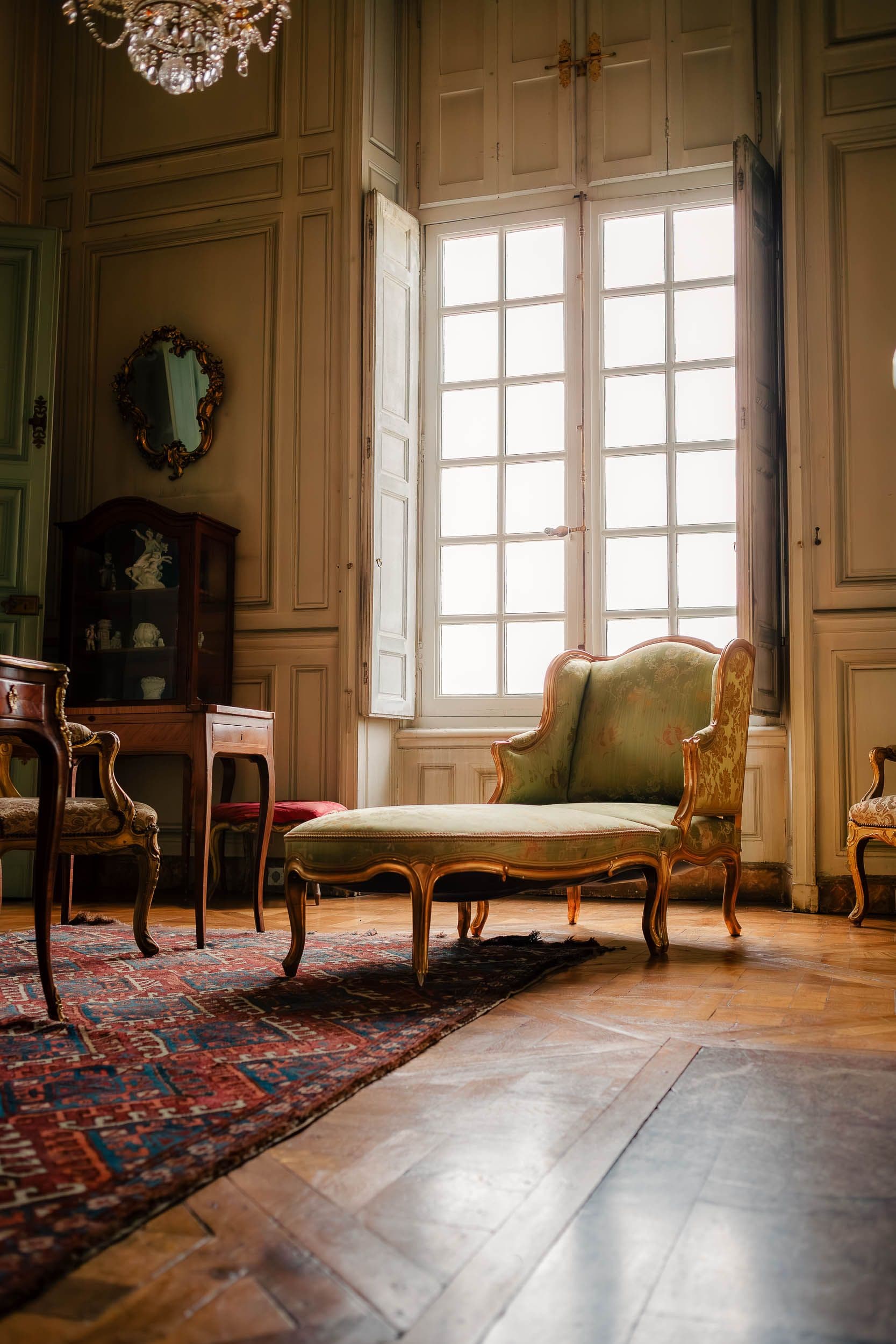 Salon classique avec fauteuils bergère verts, parquet à chevrons et hautes fenêtres, mobilier d'époque
