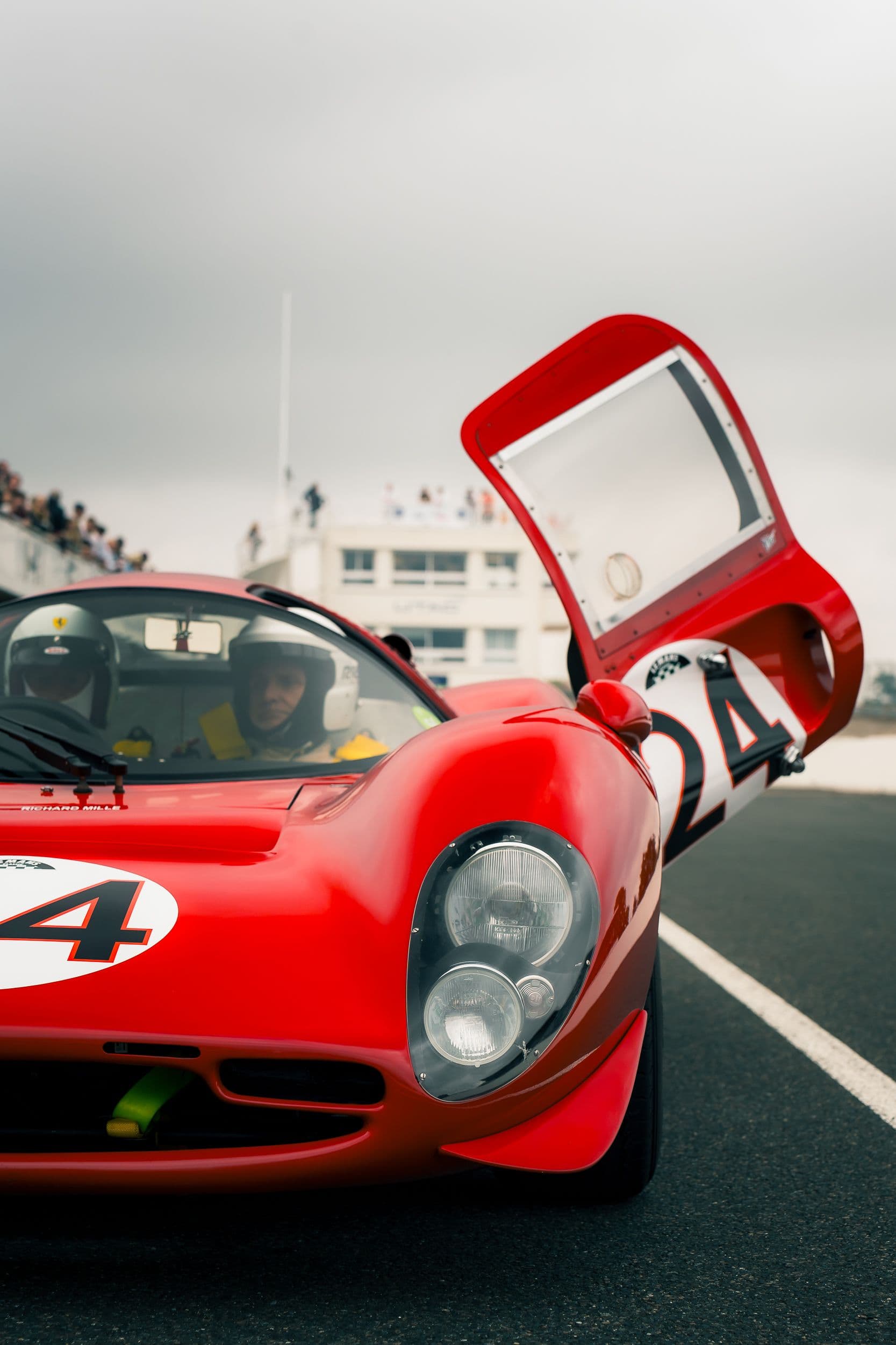 Phares avant et porte relevée numéro 24 d’une Ferrari 330 P4 Replica, avec occupants casqués.