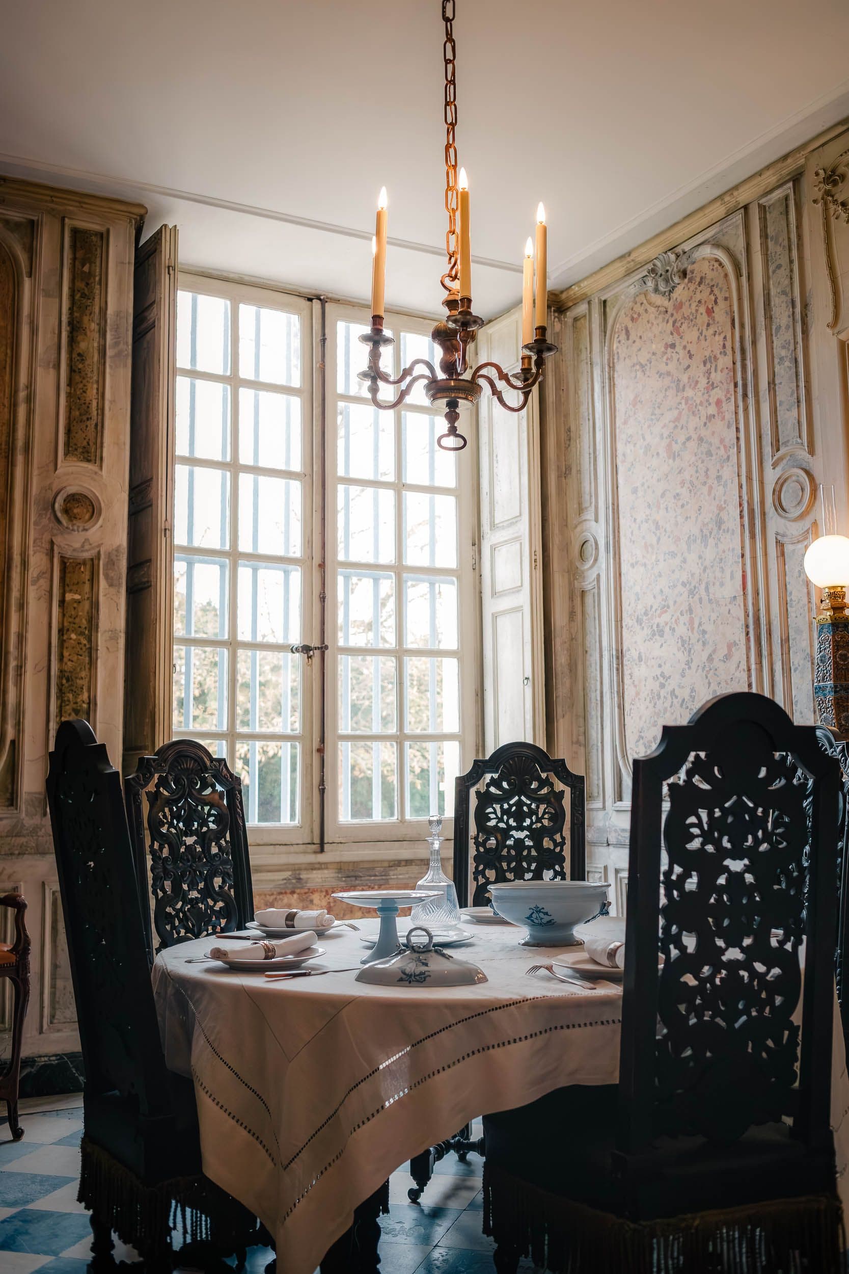 Salle à manger avec chaises baroques noires ajourées, lustre à bougies et service en porcelaine