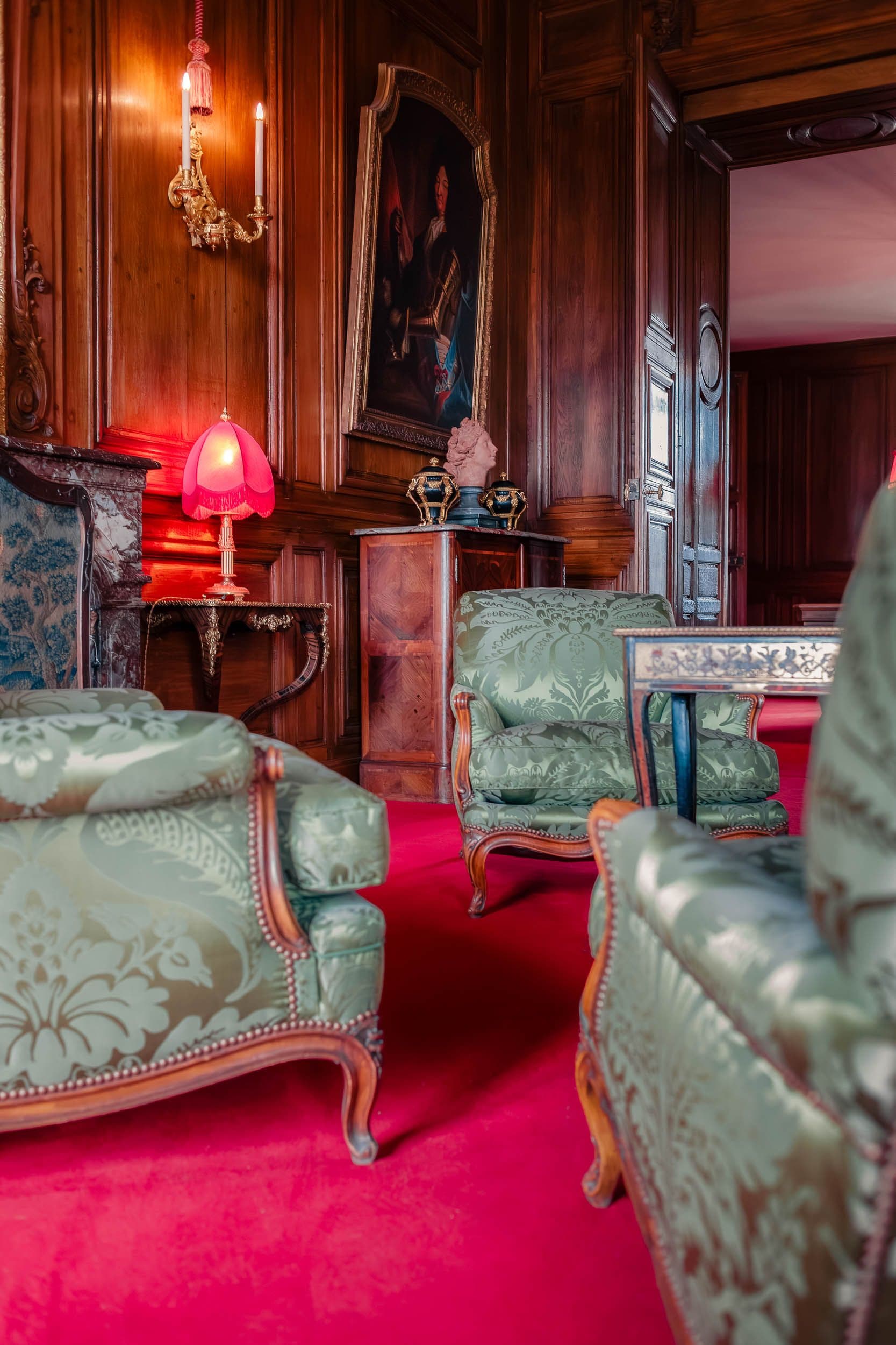 Cabinet intime avec lumière tamisée, boiseries, fauteuils verts et tapis rouge