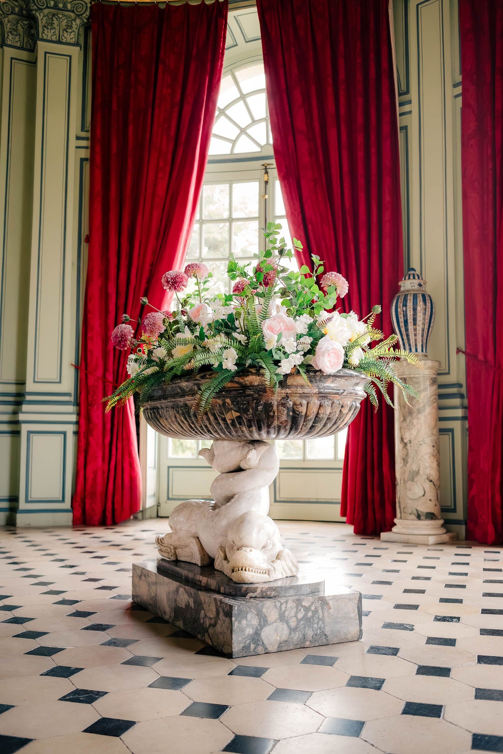 Hall d'entrée avec sculpture en marbre, composition florale et rideaux rouges velours, sol damier