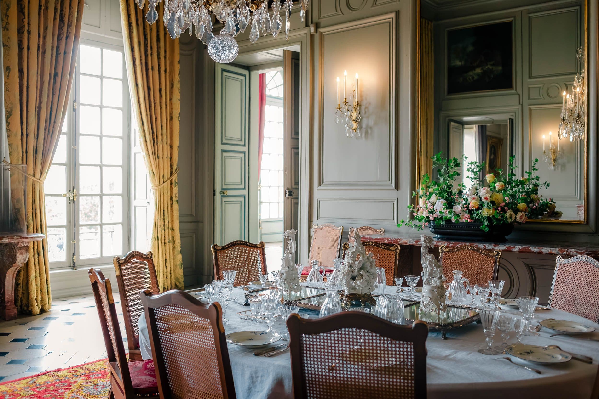 Salle à manger d'apparat avec lustre en cristal, table dressée et chaises cannées, boiseries classiques