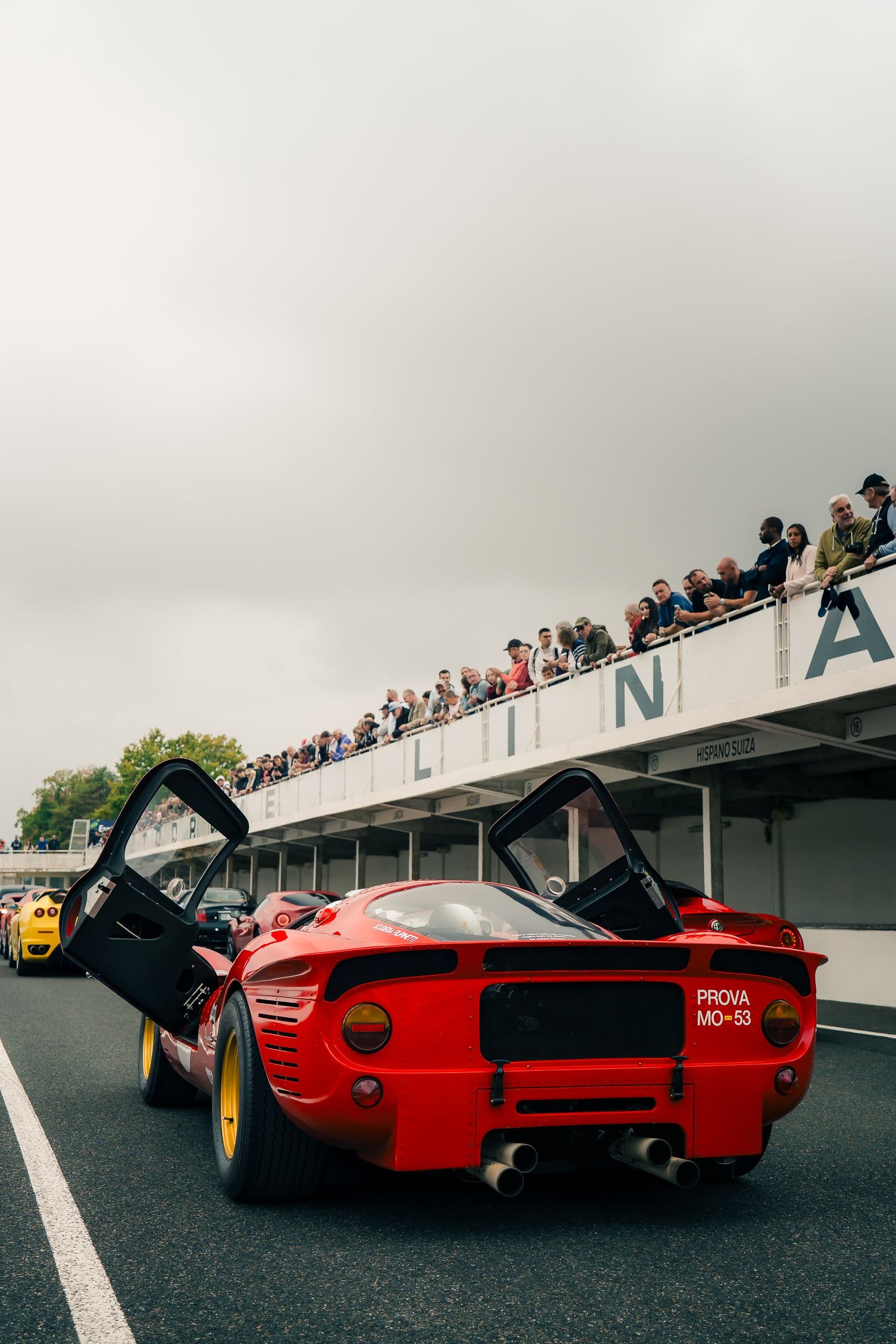 Ferrari 330 P4 Replica rouge vue de l’arrière, portes ouvertes, quatre échappements devant une file de voitures.