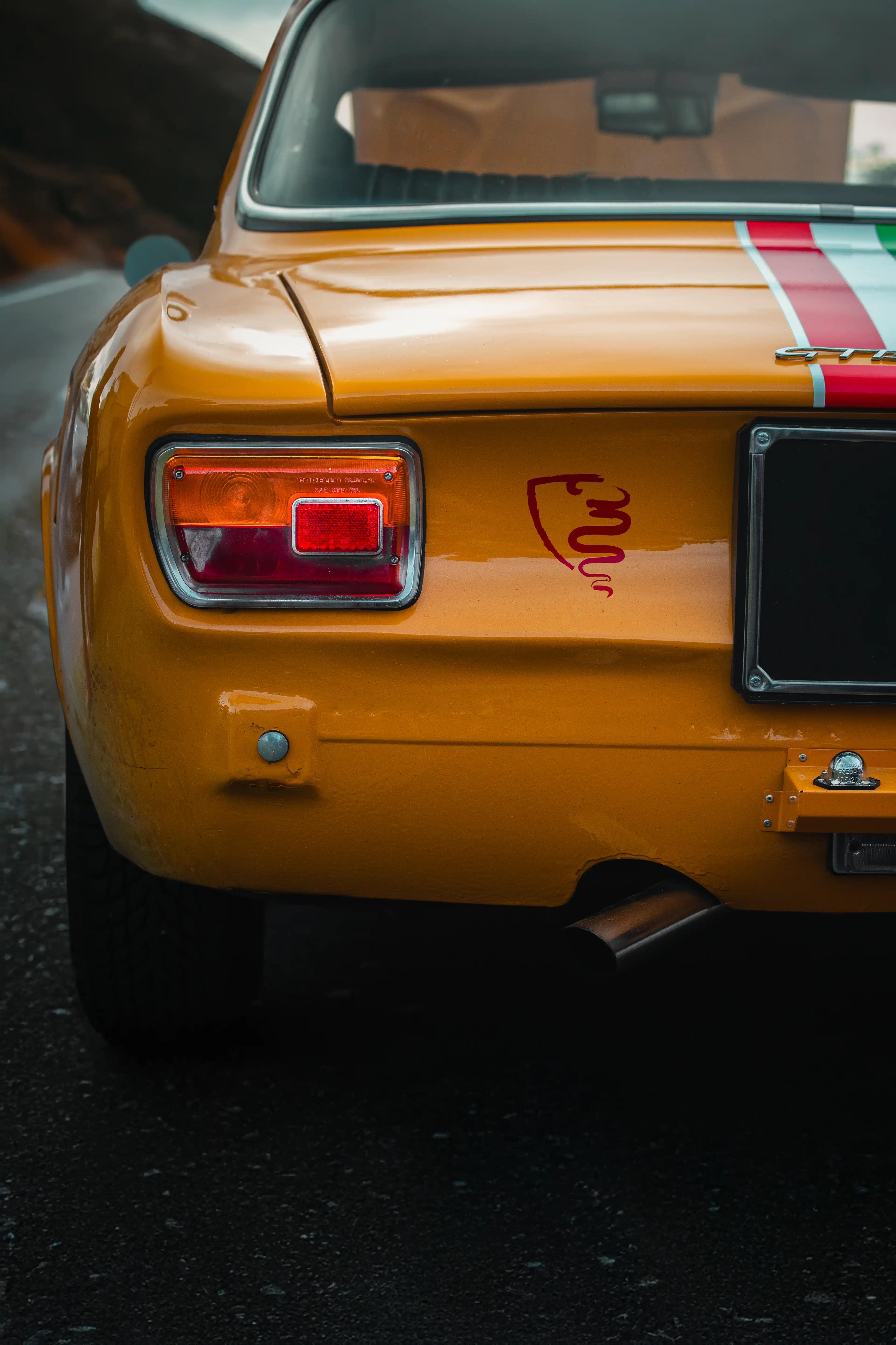 Arrière de l'Alfa Romeo GT1300 Junior jaune avec logo serpent rouge, photographie automobile classique.