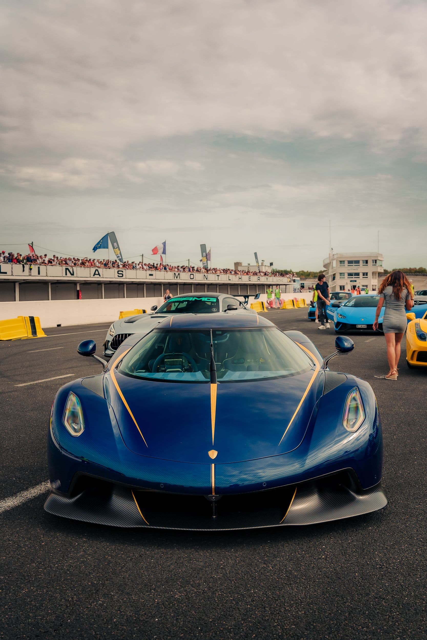 Koenigsegg Jesko bleue photographiée de face dans le paddock animé.